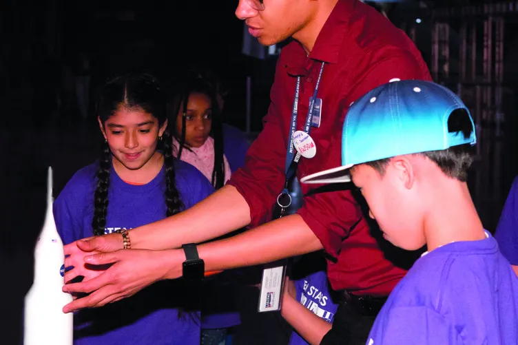 A tour guide is pointing at the nose of a space rocket in front of a group of kids.