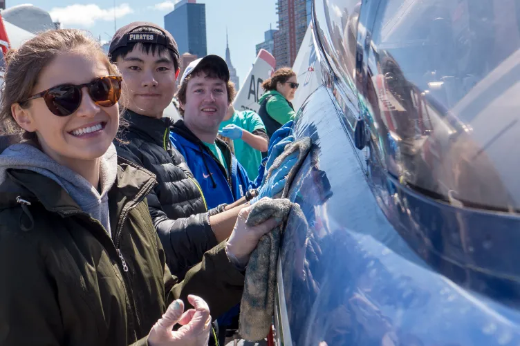 A team of corporate volunteers actively washing an aircraft on the Intrepid flight deck.