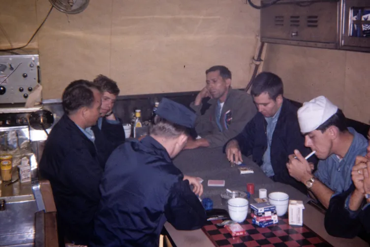 Submariners in mixed uniforms sitting around a table and playing cards in a submarine mess.