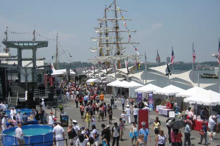 People celebrating Fleet Week on Pier 86 with tall ships docked and the Intrepid Museum