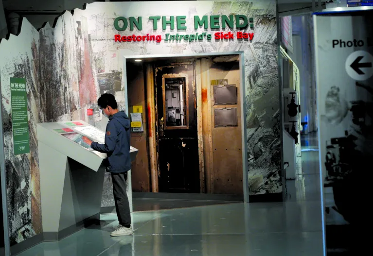 A visitor reads a panel in front of the exhibition "On the Mend: Restoring Intrepid's Sick Bay."
