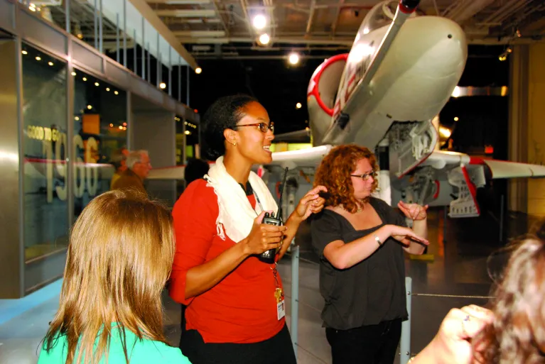 A tour guide is speaking to a group of visitors with someone translating into American Sign Language next to them.