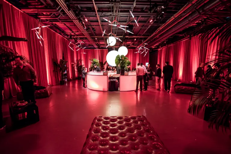 A section of Hangar 3 piped and draped, set for a small lounge space with a bar, decor and red uplighting