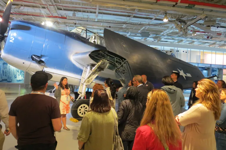 Museum educator leads a professional learning session with educators inside the hangar deck of the Intrepid Museum.