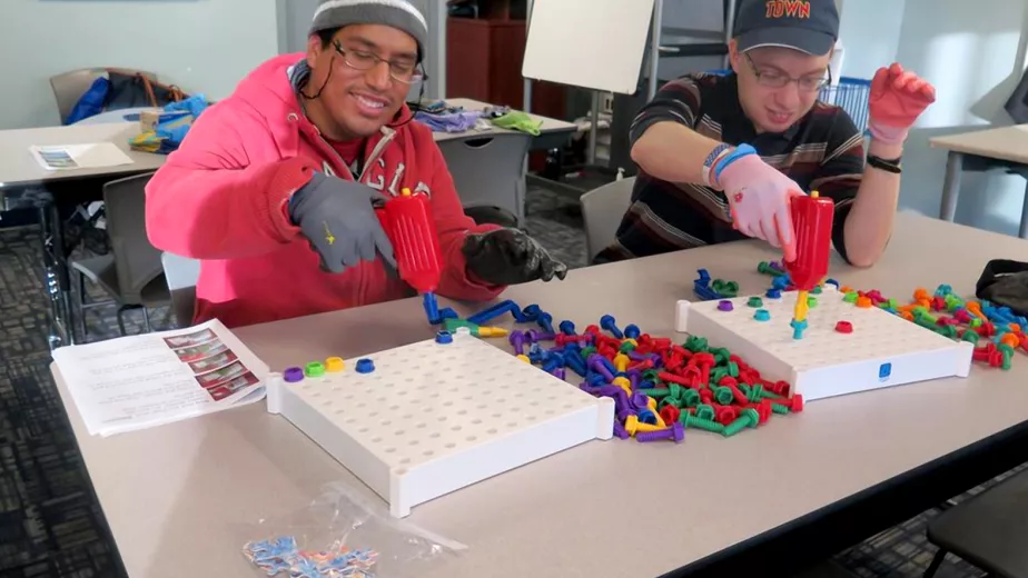 Two students are in a classroom playing with nuts and bolts toys.