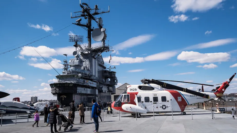 Several airpcraft on the flight deck with the island and aircraft restoration hangar in the background.