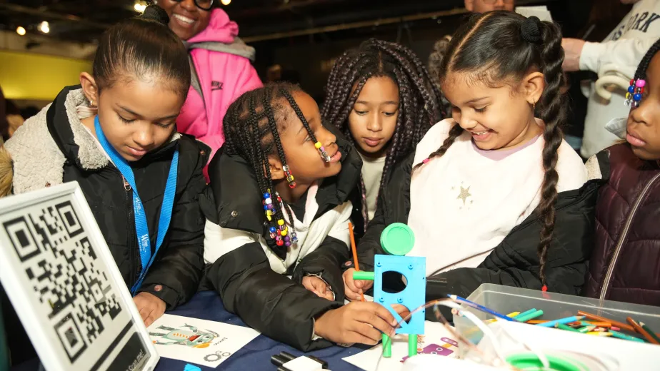 A group of children is engaged in a hands-on educational activity, examining and working on a small robot model together.