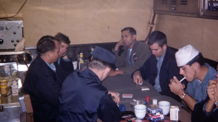 Submariners in mixed uniforms sitting around a table and playing cards in a submarine mess.