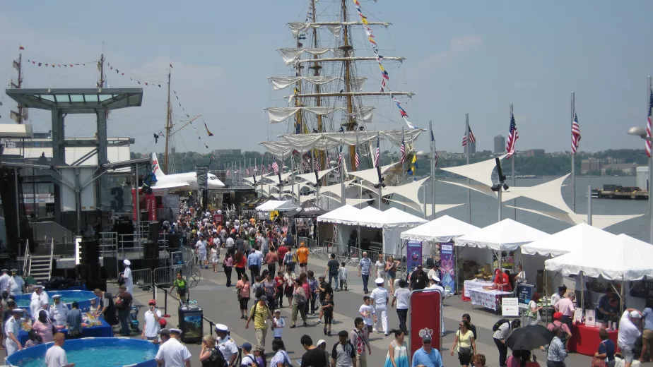People celebrating Fleet Week on Pier 86 with tall ships docked and the Intrepid Museum